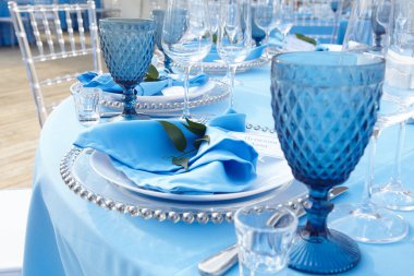 Restoranda mavi bir masa örtüsü üzerinde çatal bıçak takımı.