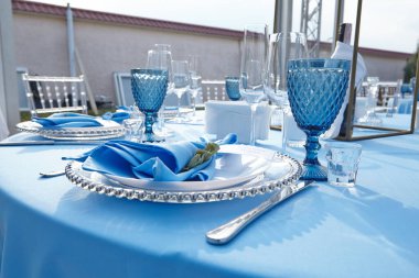 Restoranda mavi bir masa örtüsü üzerinde çatal bıçak takımı.