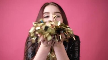 Stüdyoda pembe arka planda, parçalanmış konfetiyle genç bir kadın.