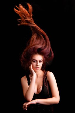 Stüdyoda uçan saçlarıyla siyah arka planda genç bir kadın.