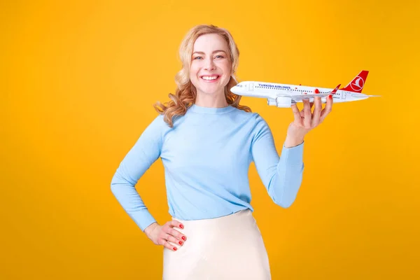Blondine Mit Weißem Flugzeug Der Hand Vor Gelbem Hintergrund Studio — Stockfoto
