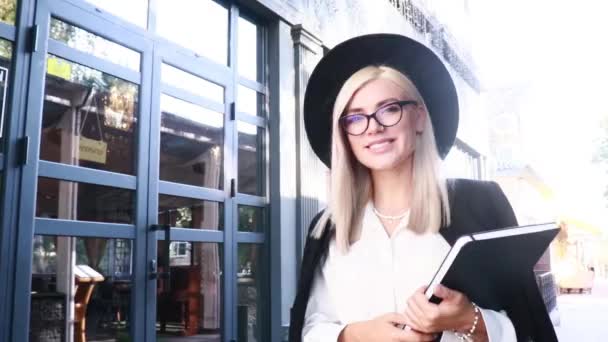 餐厅门口附近戴黑色眼镜戴黑色帽子的金发女人 — 图库视频影像