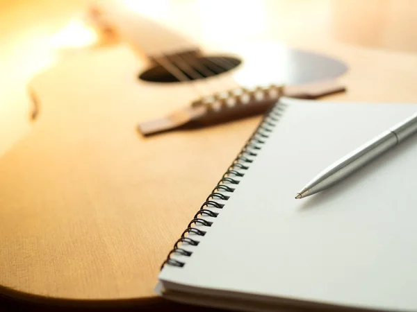 Music Creation Tools, Guitar, Notebook, and Pen on Wooden Background