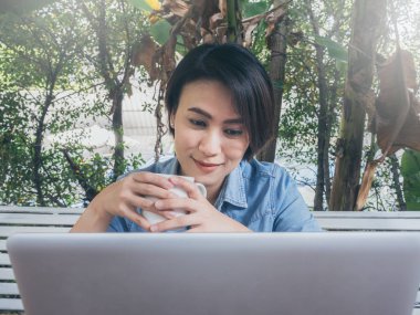 Kafede dizüstü bilgisayar kullanan güzel mutlu Asyalı kadın..