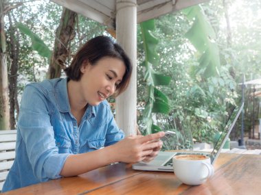 Güzel gülümseyen Asyalı kadın bilgisayarlı akıllı telefon kullanıyor.