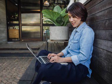 Güzel mutlu Asyalı kadın kot pantolon giyiyor ve lapto kullanıyor.