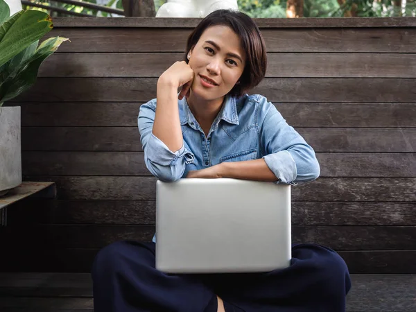 Güzel mutlu Asyalı kadın dizüstü bilgisayarlı kot gömlek giyiyor.