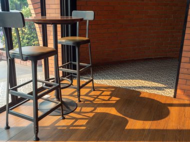Kafe dekorasyon tasarımı. Yuvarlak ahşap masa, güneş ışığı gününde cam pencerenin yanında iki modern bar taburesi var..