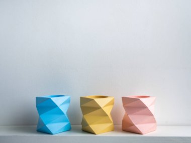 Kaktüs tenceresi. Beton çömlek. Beyaz ahşap rafta beyaz arka planda izole edilmiş üç boş mavi, pembe ve sarı modern geometrik beton saksısı var..