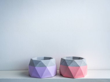 Kaktüs tenceresi. Beton çömlek. Beyaz ahşap rafta beyaz arka planda izole edilmiş iki boş pembe ve mor geometrik beton ekiciler..