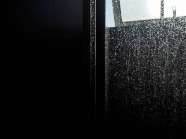 Dusty and dirty glass door. Water stain on sliding door in bathroom with copy space, dark background.