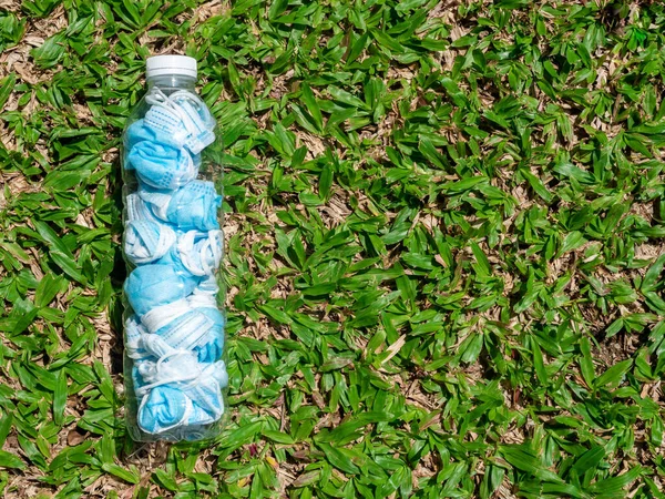 Used mask concept. Folded used protective face mask before littering for prevent spread of virus. Infect mask in the bottle on green grass background with copy space.