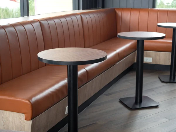 Furniture decoration in cafe retro style. Empty round wood table bars and orange long leather sofa on wood floor with natural daylight.