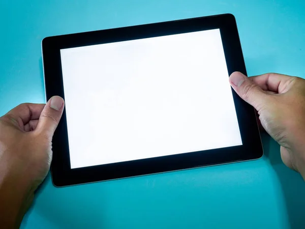 Hand holding tablet with white blank space screen on blue background, top view.