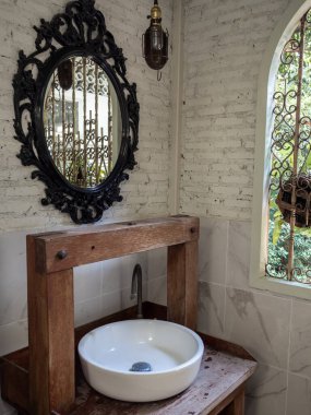 Beyaz temiz seramik lavabo banyosu ve antika ahşap masa üzerindeki musluk ve beyaz tuğlalı arka plandaki klasik ayna işlemeli pencerenin yanında dikey stil..