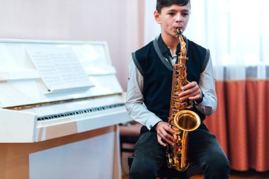 Öğrenci bir müzik dersinde otururken saksafon çalar.
