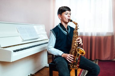 Öğrenci bir müzik dersinde otururken saksafon çalar.