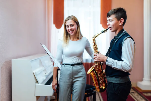 Cheerful teacher with student boy learning saxophone lessons at — Stock Photo, Image