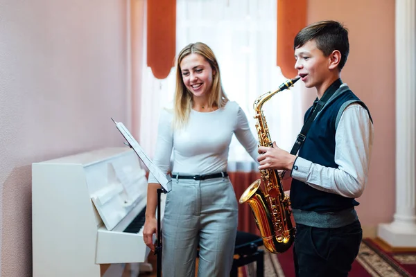 Alegre maestro con estudiante niño aprendiendo lecciones de saxofón en —  Fotos de Stock