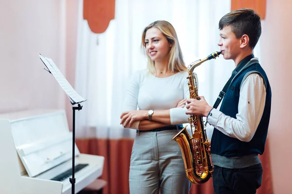 Cheerful teacher with student boy learning saxophone lessons at — Stock Photo, Image