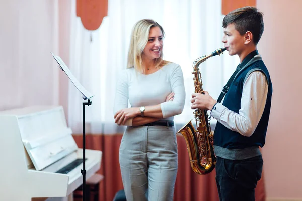 Cheerful teacher with student boy learning saxophone lessons at — Stock Photo, Image