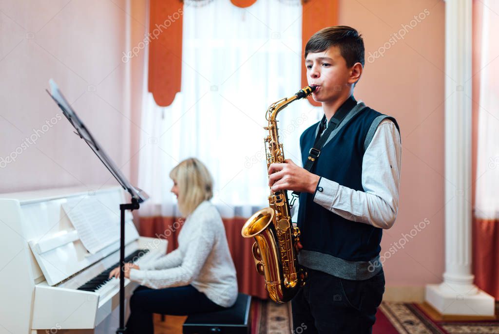 A teenage boy learns to play saxophone in a music lesson to acco