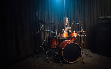 Kadın konser sırasında davul ve ziller çalıyor. Sahnedeki bando karanlıkta. Yukarıdan bir noktayla aydınlatılıyor.