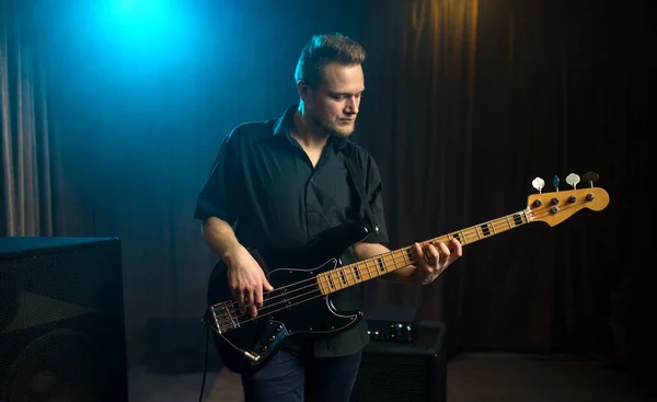 コピースペースのある青いスポットライトに照らされたライブパフォーマンス中にステージでエレキバスギターを演奏する男性ギタリスト — ストック写真