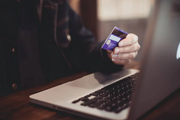 Kredi kartı tutan ve dizüstü bilgisayar kullanarak el. Online alışveriş kavramı