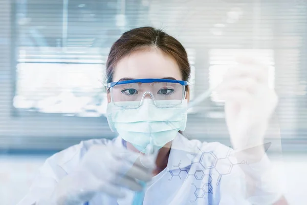 Female Scientist or Doctor With Green Solution In Laboratory - Stock Photo A female doctor or medical examiner looking at a test tube of a green solution in a laboratory.