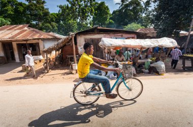 Stone Town, Zanzibar - Mayıs 15-2015: genç adam arka plan meyve ahır ile köy yolu boyunca onun bisiklet sürme.