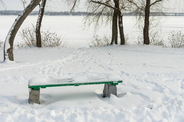 Winter landscape with empty bench in deep snow on a Dnipro riverside, Ukraine