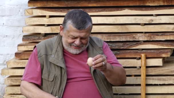 积极的乌克兰高级男子饮用生母鸡的鸡蛋 而坐在户外对桩板 — 图库视频影像