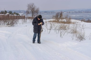 Olgun adam Ukrayna donmuş Dnipro Nehri yakınında bir karlı yolda yürürken cep telefonu kontrol