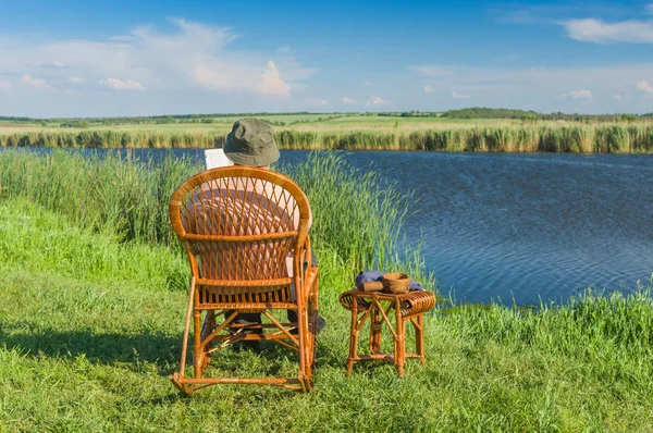 Komuta sizde yaz sezonunda bir riverside hasır sallanan-sandalyede otururken kitap okuma