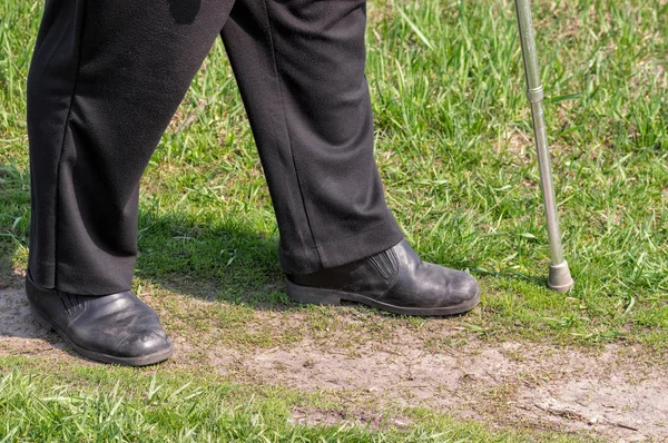 Man with walking stick wearing old scratched shoes walking on an earth road