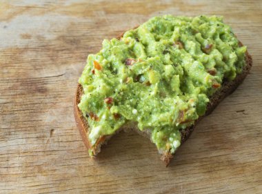 Tahta bir tahtanın üzerinde duran guacamole soslu sandviç.