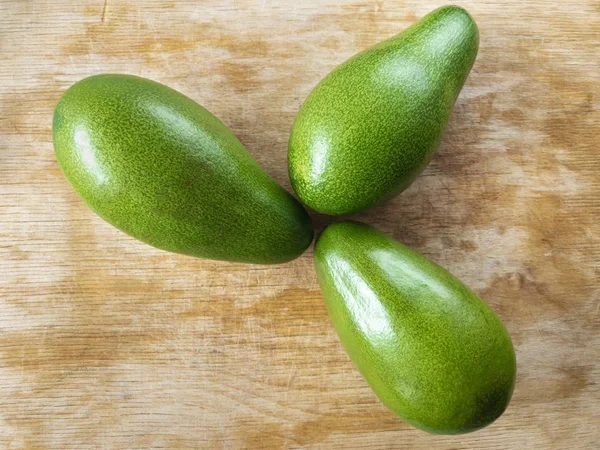 Draufsicht auf drei Avocados, die auf einem Holzbrett liegen — Stockfoto