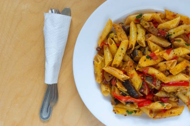 Sebzelerle pişirilmiş makarna dolu beyaz tabakta üst manzara.