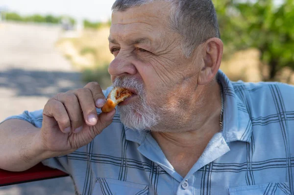 Hungry senior driver eating patty filled with fried cabbage near his car on a summer road
