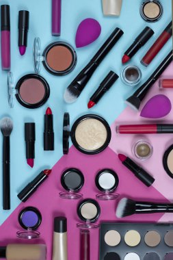 Makyaj seti, ruj, dudak parlatıcıları, kremler, temel, allık, pudra, fosforlu kalem ve göz farı içeren pembe ve mavi arka plan görünümlü bir makyaj seti. düz yat