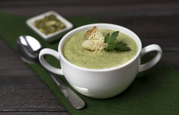 Vegetarische room van broccoli, aardappel, ui, knoflook, sesam en olijfolie, en kokosmelk soep. geserveerd in een witte keramische plaat op een donkerbruine houten plaat met groen textiel — Stockfoto