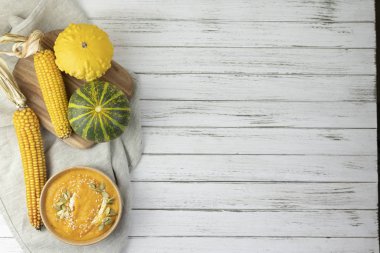 Balkabağı kremalı çorba beyaz ahşap bir arka planda açık gri tekstil, balkabağı parçaları, tohumlar, mısır. Düz yat. Boşluğu kopyala.