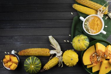 Koyu ahşap bir zeminde, beyaz seramik tabakta balkabağı kremalı çorba. Yeşil tekstil, balkabağı parçaları, tohumlar, mısır. Düz yat. Boşluğu kopyala.