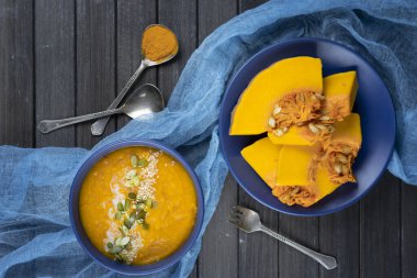 Koyu ahşap zemin üzerinde seramik bir kasede balkabağı kremalı çorba mavi tekstil, balkabağı dilimleri kullanarak. düz yat.