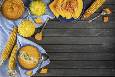 Mavi tekstil, tencere, dekoratif balkabağı, mısır ve çatal bıçak kullanarak koyu ahşap bir zeminde seramik bir kasede balkabağı kreması çorbası. Düz yat. Boşluğu kopyala.