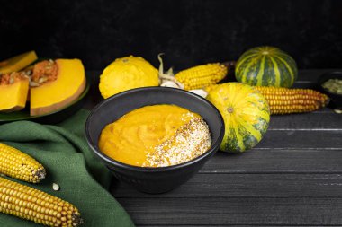 Yeşil tekstil, balkabağı parçaları, tohumlar, mısır kullanarak siyah seramik tabakta balkabağı kremalı çorba. Düz yat. Boşluğu kopyala.