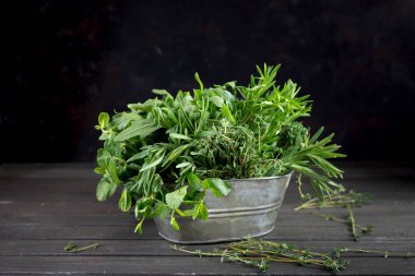 Taze kokulu yeşil otlar, siyah ahşap bir arka planda, metal bir kasede. Biberiyeli kekik fesleğen, naneli ıspanak, salata, roka. sıfır atık kavramı
