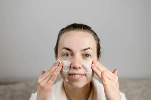 european woman applies cream, mask to the face. home spa concept.