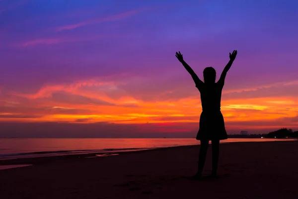 Silueta de mujer con las manos en alto mientras está de pie en la playa del mar en — Foto de Stock